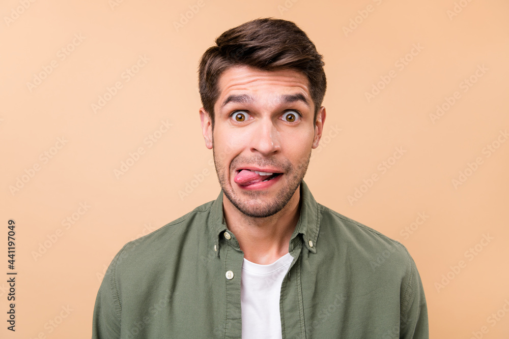 Photo of fooling funky young man make funny face stick out tongue isolated on pastel beige color background