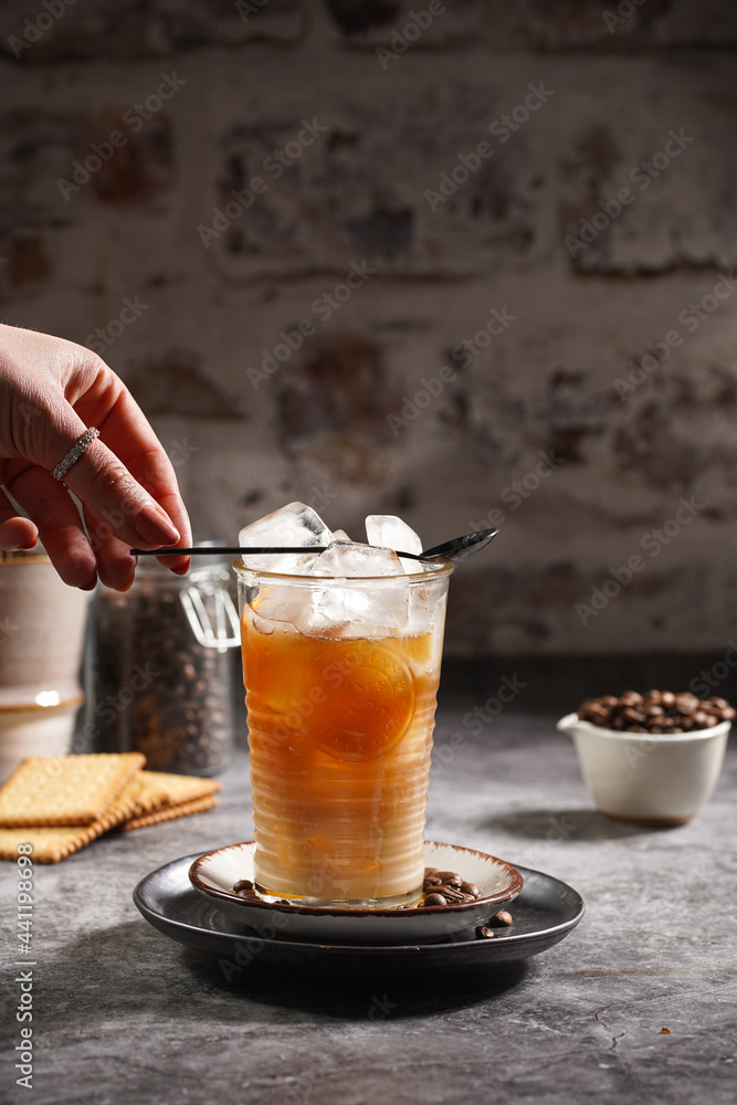 Female hand putting black tea spoon on a glass with ice cubes and coffee Female hand putting black tea spoon on a glass with ice cubes and coffee