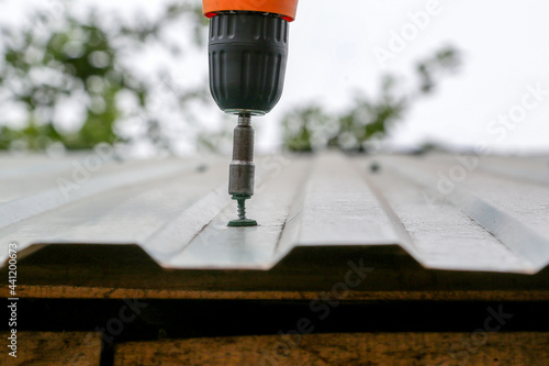 male builder performs work on the roof, fastens corrugated sheets
