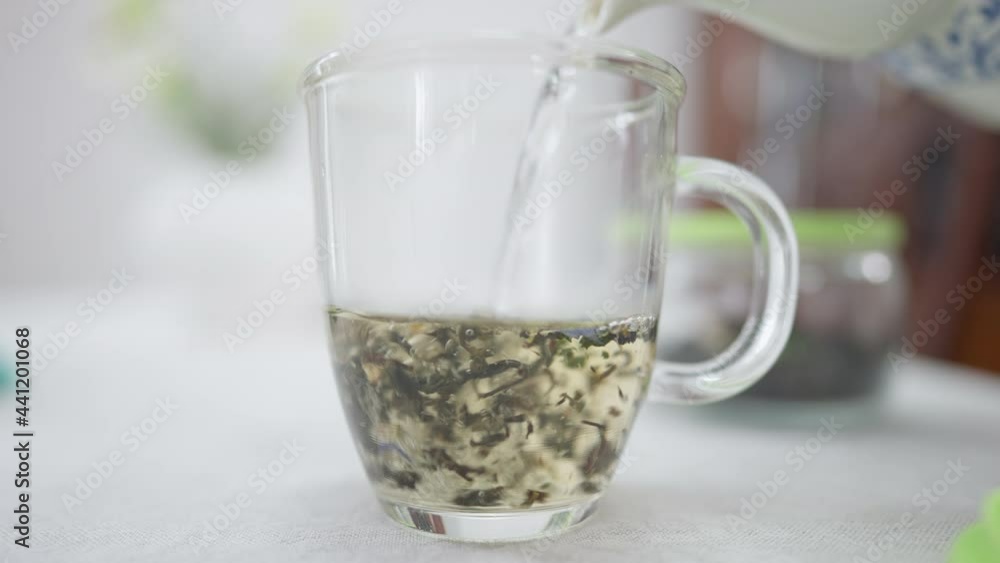 Close-up hot water pouring in transparent cup with tea leaves. Brewing of healthful detox organic drink indoors Close-up hot water pouring in transparent cup with tea leaves. Brewing of healthful detox organic drink indoors