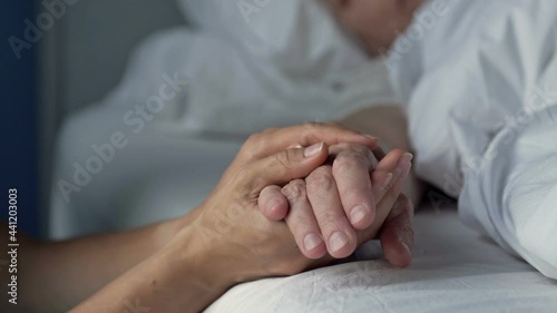 Caring young hand holding the hand of an old and sick loved one. Love, compassion and family support. Close-up.