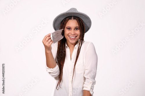 Attractive woman wearing hat putting on mask on white background 