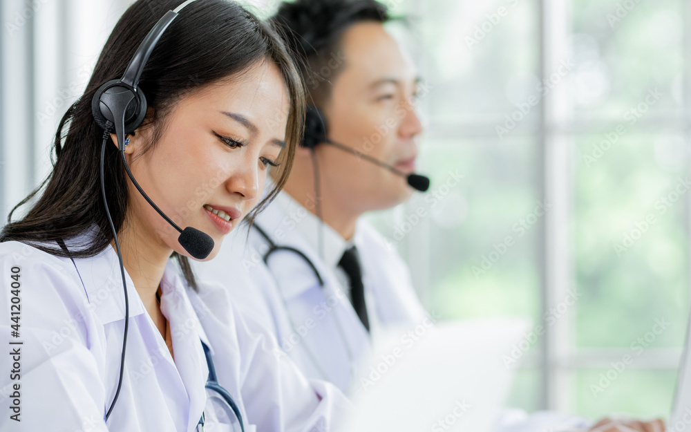Portrait Asian beautiful female doctor smiling with headsets, sitting and looking at computer screen, making online telemedicine, giving service, advise medicines or medical treatment to patients. Portrait Asian beautiful female doctor smiling with headsets, sitting and looking at computer screen, making online telemedicine, giving service, advise medicines or medical treatment to patients.
