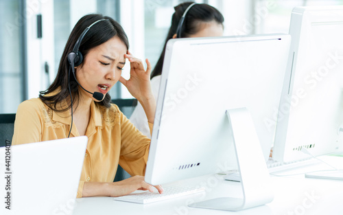 Asian beautiful attractive female call center stressful working with pressure with headsets, sitting, monitoring at computer screen in agency, giving service and receiving complaints of customers. photo