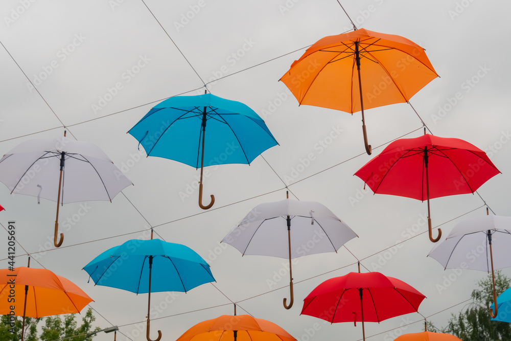Low angle view: colorful umbrellas hanging against gray overcast sky and swaying in wind at summer city festival. Street decoration, celebration, art, holiday concept