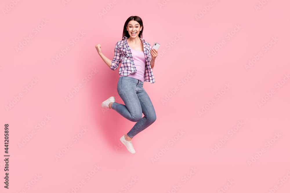 Full length body size photo girl in checkered shirt keeping cellphone gesturing like winner isolated pastel pink color background