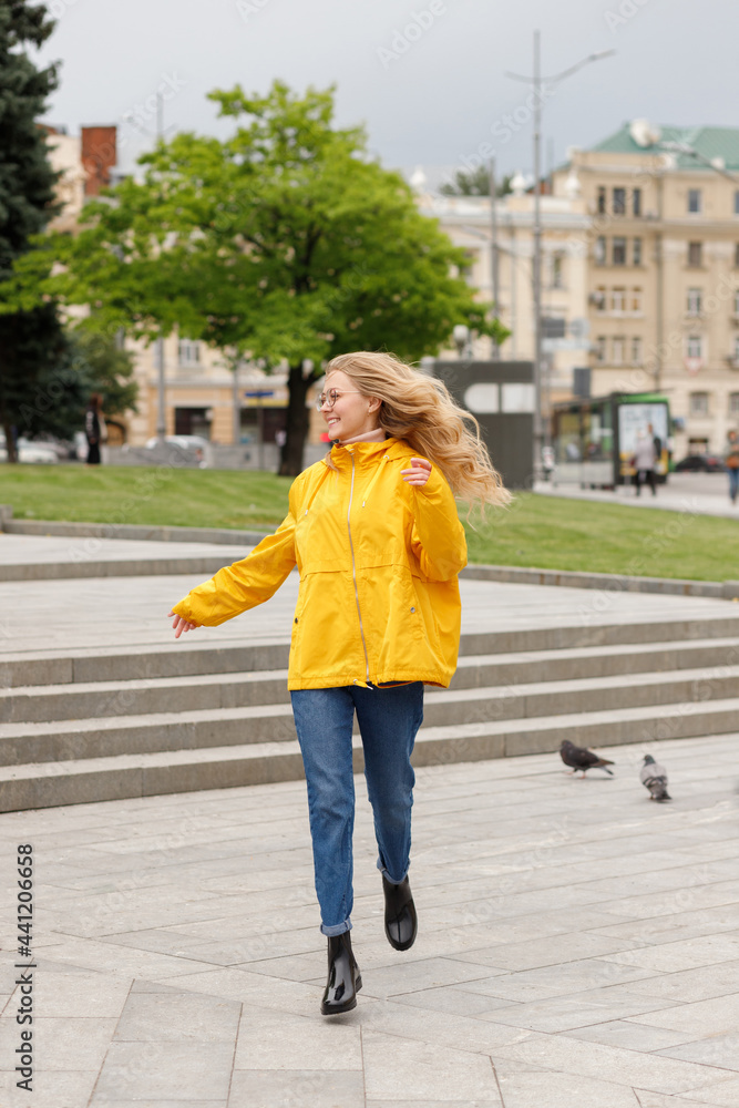 Woman with long hair in yellow raincoat runs and smiles around the city on a walk