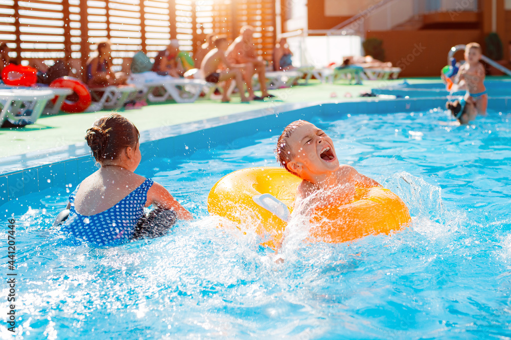 Kid boy playing outdoor pool of resort. in an inflatable yellow circle with a ball. Children frolic with water toys.
