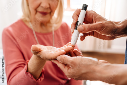 A close-up view of the doctor measuring blood glucose level to her elderly patient
