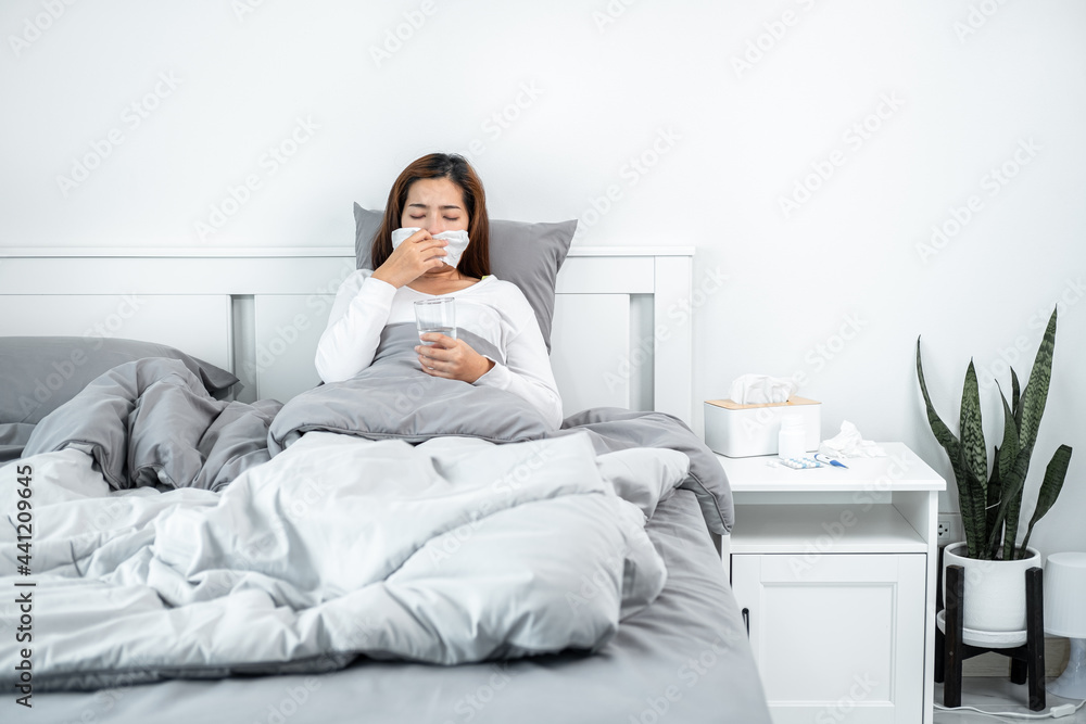 Asian woman using tissue to cough, sneeze and holding a glass of water to take medicine while feeling sick Asian woman using tissue to cough, sneeze and holding a glass of water to take medicine while feeling sick