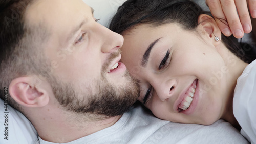 happy brunette woman leaning on bearded boyfriend while resting on bed.