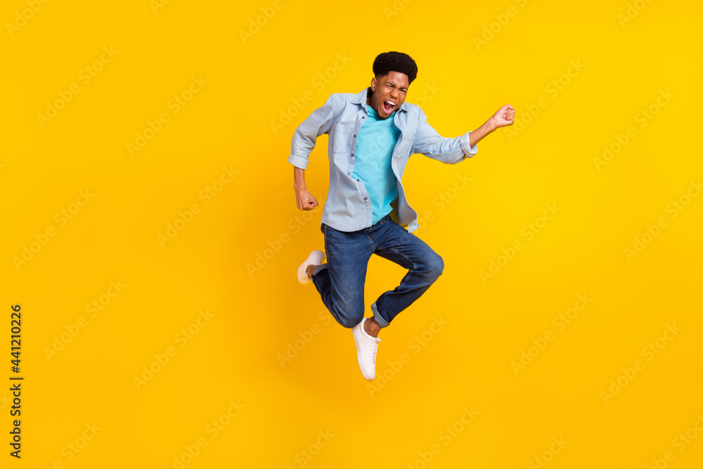 Photo of funky excited dark skin man wear jeans shirt jumping high running fast isolated yellow color background