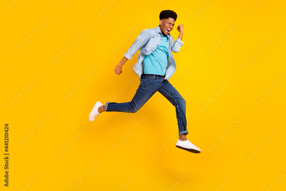 Photo of funky charming dark skin man wear jeans shirt jumping high running fast isolated yellow color background Photo of funky charming dark skin man wear jeans shirt jumping high running fast isolated yellow color background