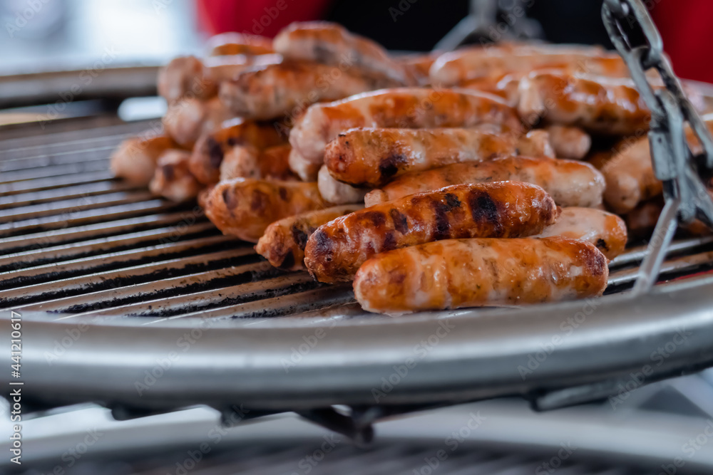 Process of grilling fresh meat sausages on big round hanging grill at summer local food market: close up view. Outdoor cooking, barbecue, gastronomy, cookery, street food concept