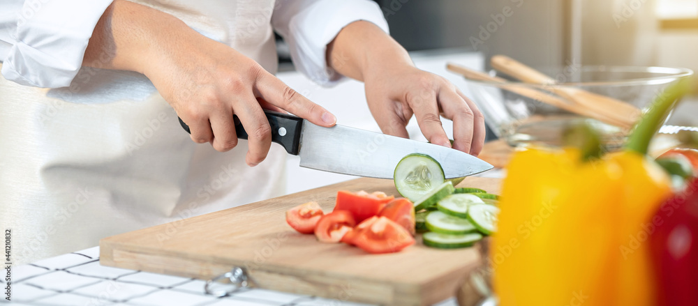 Close up of asian housewife wearing apron and using knife to slice cucumber and tomato on chopping board Close up of asian housewife wearing apron and using knife to slice cucumber and tomato on chopping board
