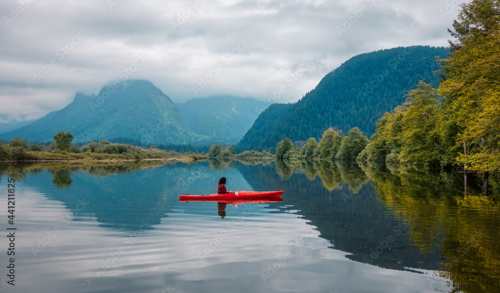 Adventure Caucasian Adult Woman Kayaking in Red Kayak surrounded by Canadian Mountain Landscape. Artistic Color Render. Taken in Widgeon Valley, Pitt Meadows, Vancouver, British Columbia, Canada.