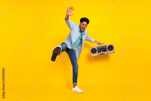 Photo of cool charming dark skin man wear jeans shirt listening boombox singing dancing isolated yellow color background
