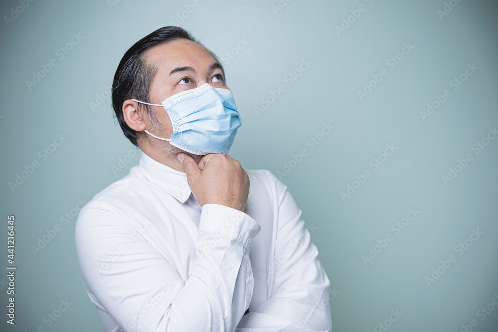 Asian businessman wearing a white shirt and wear a medical mask to prevent the coronavirus. Looking above, thinking about his own business. Social distancing, a new normal concept.