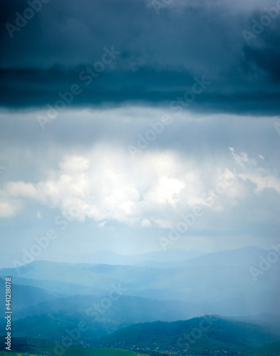 A village in the Carpathian mountains in the rays of light against the background of rain clouds. Rest and travel in the mountains.