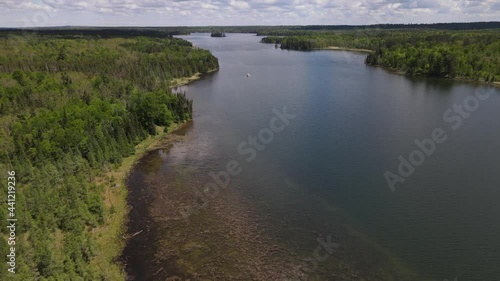 4K flyover of beautiful blue lake showing cloud reflections and pontoon boats on lake. Vibrant green treed shoreline surrounding water. Lake Itasca, MN. 
