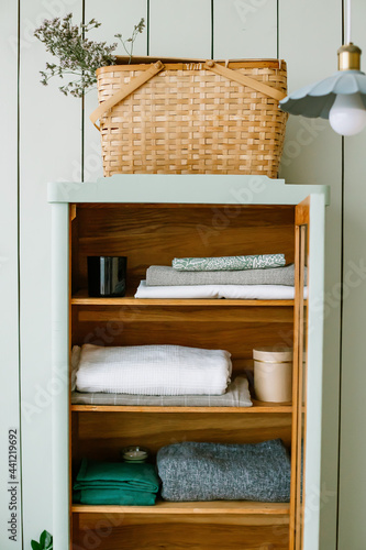 Scandinavian style wooden wardrobe with bed linen and candles inside mixed fabrics Shelves for clothes Basket with flowers and a lamp