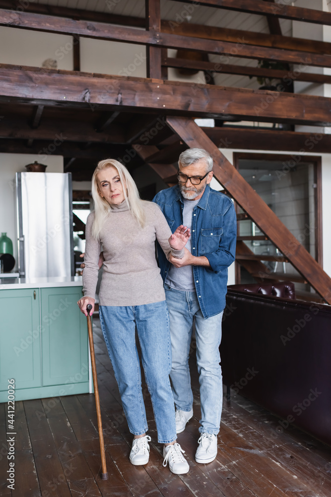 Fototapeta premium Senior woman with crutch standing near careful husband at home