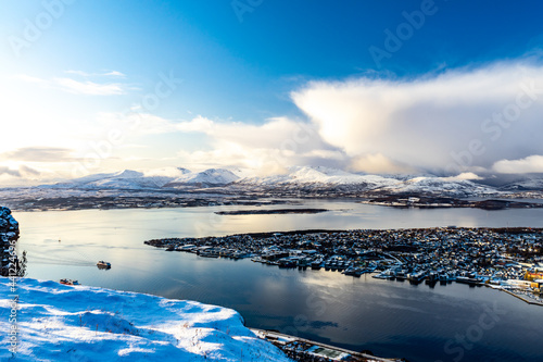 Die Insel von Tromsö im blauen Fjord vom Fjellheisen aus gesehen. erster Schnee im Herbst mit Gewitterwolken im Hintergrund. abwechslungsreiches Wetter in Troms, Norwegen