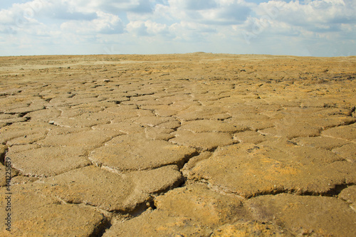 Dried, cracked brown clay surface. The surface extends far beyond the horizon. A bright, sunny day. Angle view. In the background, a blue sky with clouds.