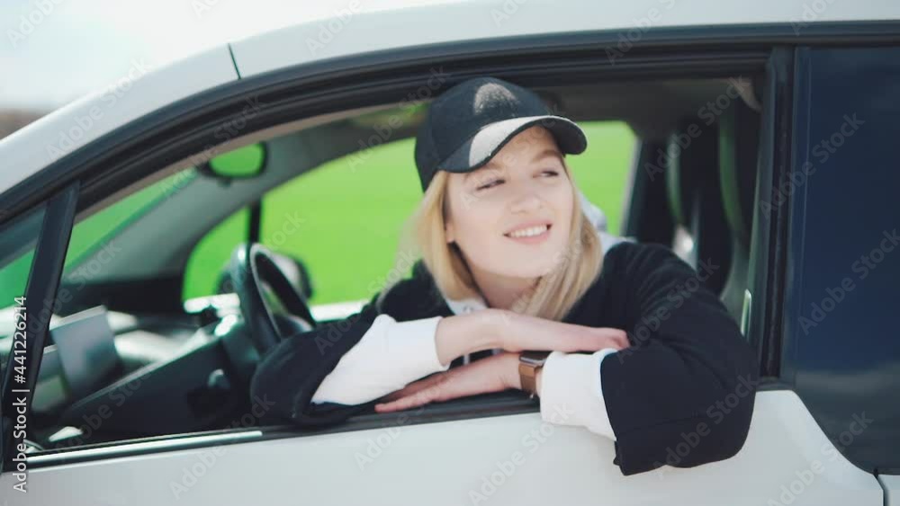 Young attractive girl in a black cap sits in an electric car and smiles at the camera Young attractive girl in a black cap sits in an electric car and smiles at the camera
