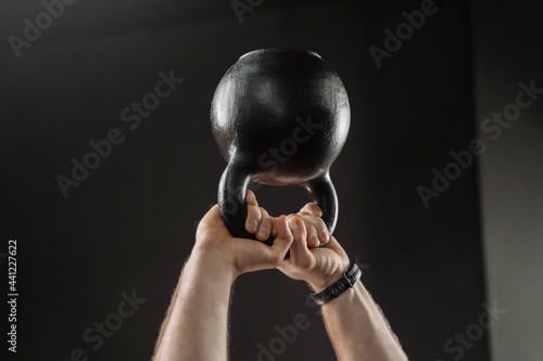 Close up of muscular man's hands holding heavy kettlebell overhead. Hands holding heavy kettle bell for strength training exercise. Workout, fitness and crossfit concept photo