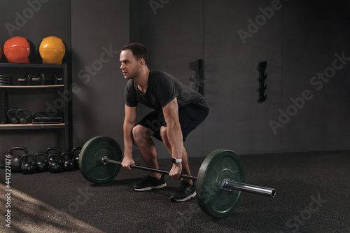 Crossfit athlete squatting and preparing to lift heavy barbell while training weightlifting. Fit young man lifting weight, working out at gym. Dark background. Sport, fitness, powerlifting concept