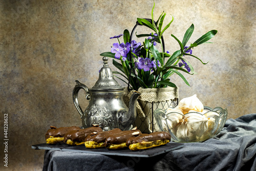 french desserts : eclairs with custard and chocolate icing decorated with hazelnuts and Meringue prepared from whipped with sugar and baked eggs with teapot on table 