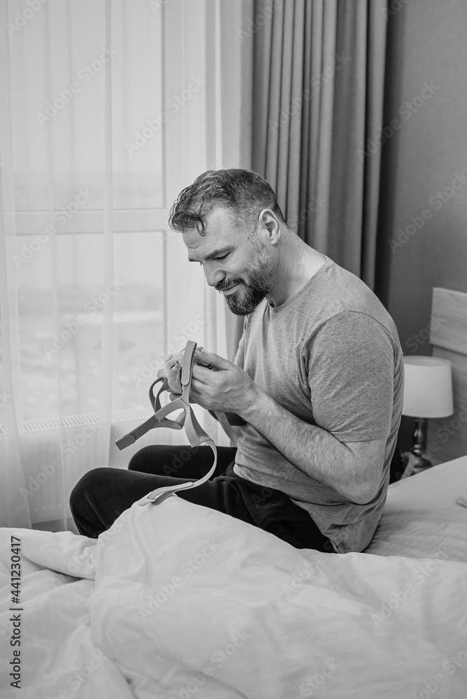 monochrome portrait of Happy rested man with chronic breathing issues after using  CPAP machine sitting on the bed in bedroom. Healthcare, CPAP, Obstructive sleep apnea therapy, snoring concept