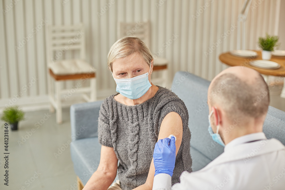 Man doctor vaccinates an elderly woman at her home wearing a protective mask. Vaccination concept Man doctor vaccinates an elderly woman at her home wearing a protective mask. Vaccination concept