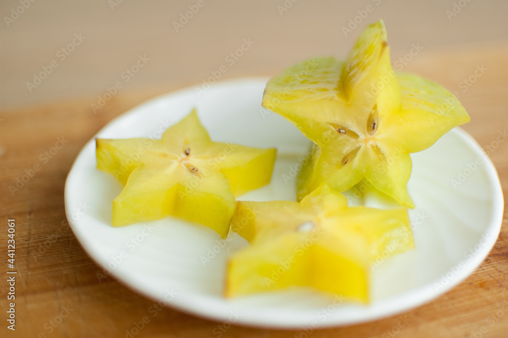 Exotic starfruit or averrhoa carambola on white plate on wooden cut board. Healthy food, fresh organic star apple fruit. Exotic starfruit or averrhoa carambola on white plate on wooden cut board. Healthy food, fresh organic star apple fruit.