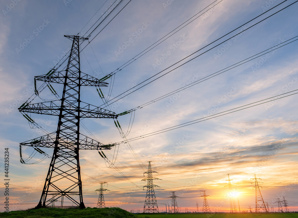 silhouette of high voltage power lines against a colorful sky at sunrise.