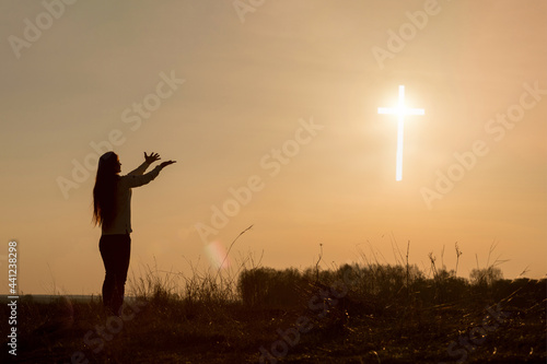 Fototapeta Naklejka Na Ścianę i Meble -  Woman raised her hands up in front of a glowing cross .