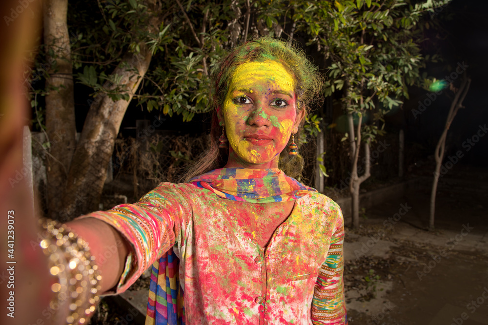 Young girl with colorful face taking selfie using smartphone or Camera on Holi festival. Festival and technology concept. Young girl with colorful face taking selfie using smartphone or Camera on Holi festival. Festival and technology concept.