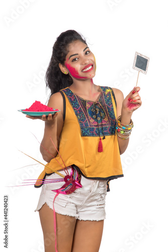Beautiful young girl holding powdered color in a plate with a carnival mask and small signboard on the occasion of the Holi festival.