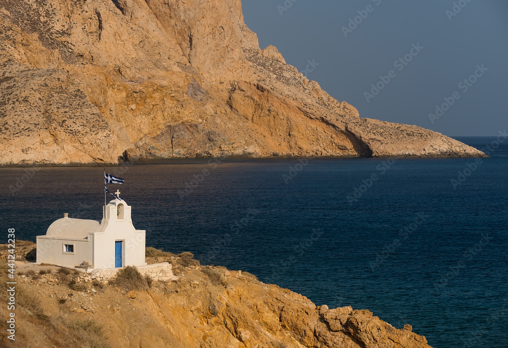 Small church and sailboat at anchor in the bay on the south coast of the Greek island of Anafi, in the background the impressive Mount Kalamos massif