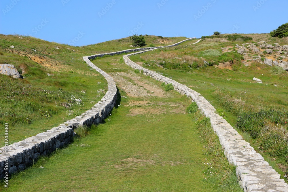A low stone wall lined curving path through public land next to the sea Suances Cantabria Spain May 2021