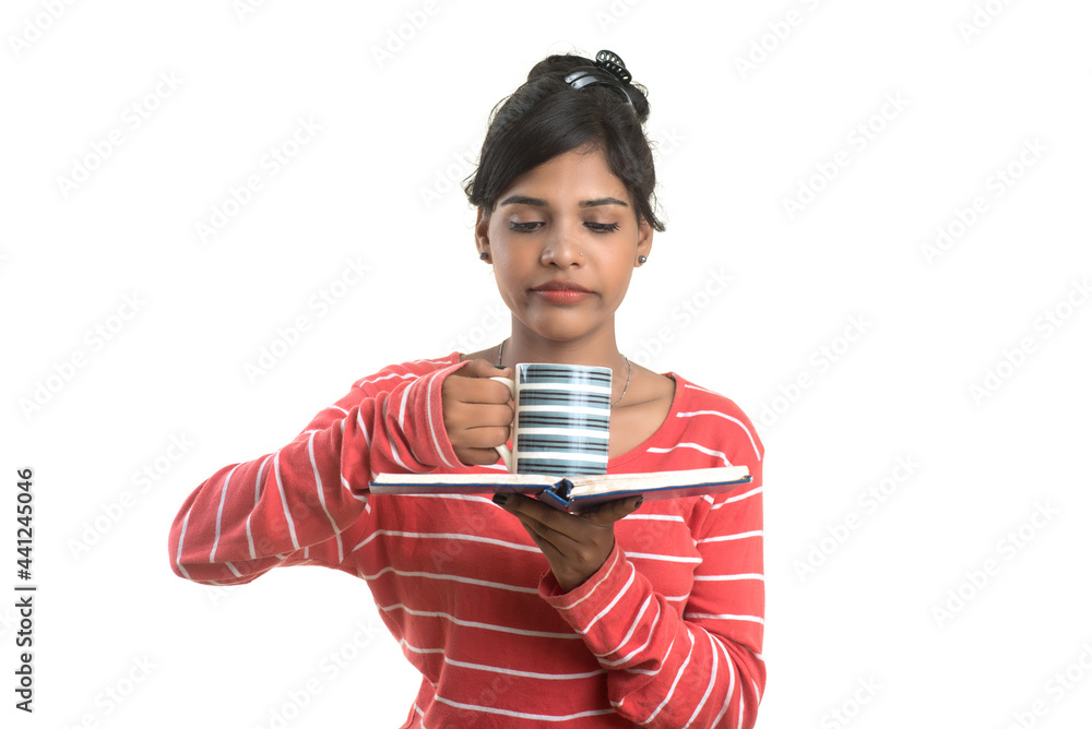 Naklejka premium Beautiful young girl with book and cup of coffee posing on a white background.