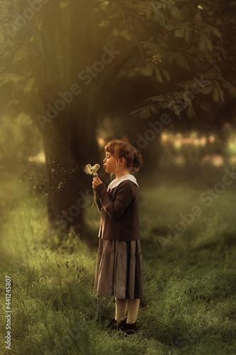 girl in retro clothes stands in a summer park and blows on a dandelion