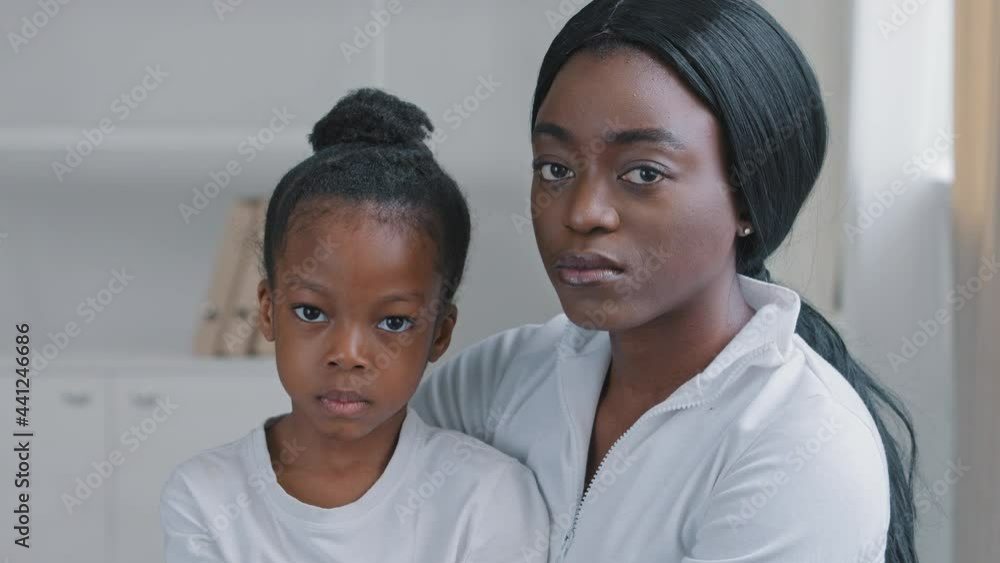 Family portrait sad african american mother caring ethnic woman and upset serious little afro daughter black preschooler child girl sitting hugging looking at camera with worried expression indoors Family portrait sad african american mother caring ethnic woman and upset serious little afro daughter black preschooler child girl sitting hugging looking at camera with worried expression indoors