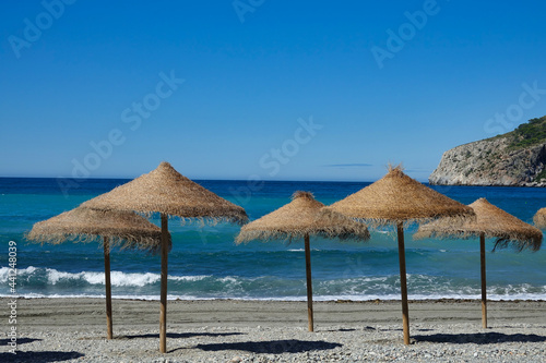Fototapeta Naklejka Na Ścianę i Meble -  Straw umbrellas on the shore of an Andalusian Mediterranean beach