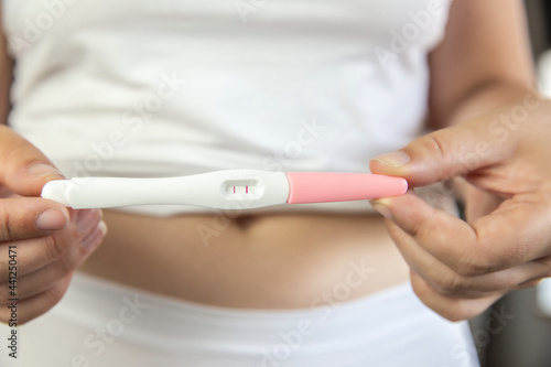 Young women wearing white underwear with hand holding positive result pregnancy test and belly.