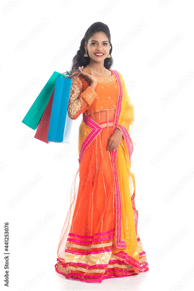 Fototapeta premium Beautiful Indian young girl holding shopping bags while wearing traditional ethnic wear. Isolated on a white background