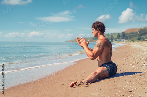 Athletic man with beautiful muscles sits on a twine in summer training at seashore