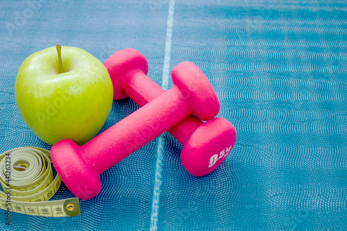 Two red dumbbells, an apple and a centimeter ribbon on a yoga mat. Concepts about fitness, sport and health.