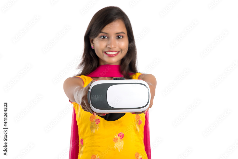 Indian traditional young girl holding and showing VR device, vr box, goggles, 3D Virtual Reality Glasses headset, Girl with Modern imaging Future technology on white background. Indian traditional young girl holding and showing VR device, vr box, goggles, 3D Virtual Reality Glasses headset, Girl with Modern imaging Future technology on white background.